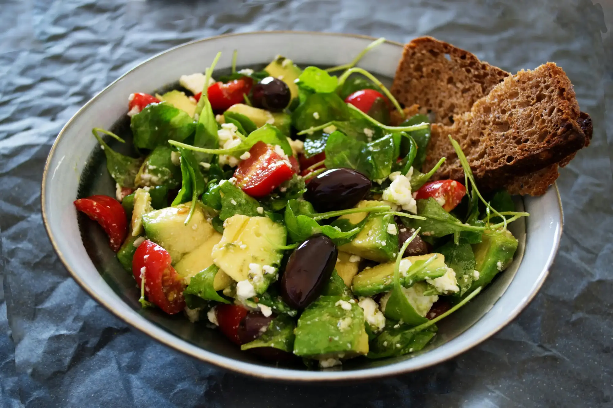 Avokado, roka, cherry domates, zeytin ve peynir ile hazırlanmış sağlıklı avokadolu salata yanında tam buğday ekmeği