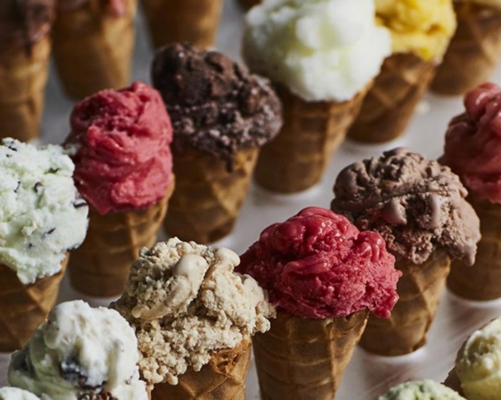 Yakın çekim bir karede, çıtır waffle külahları içinde sunulan vanilya, çikolata, çilek, fıstık ve karamel gibi birçok farklı renkte ve lezzette dondurma topu, keyifli bir yaz gününü çağrıştırıyor.