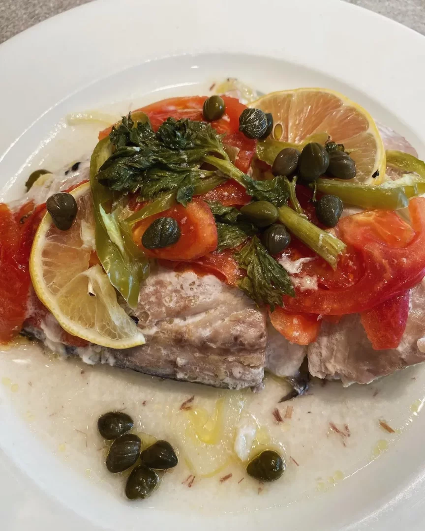 Karaköy Lokantası'nda servis edildiği anlaşılan, domates, yeşil biber, kapari, limon dilimleri ve taze yeşilliklerle zenginleştirilmiş, hafif kremalı sos eşliğinde sunulan beyaz balık yemeği tabağı.