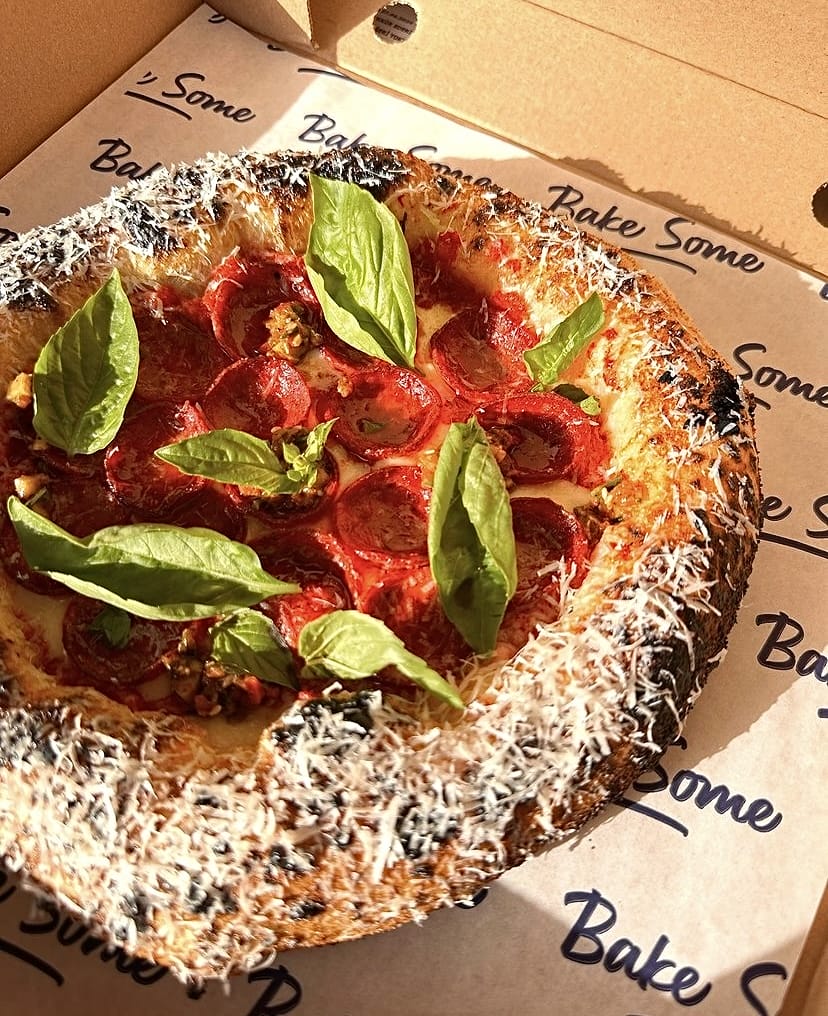 Bake Some'un İzmir'deki eşsiz pastaneler ve bakeryler rehberinde öne çıkan, kalın kenarlı ve hafifçe yanık kenarları rendelenmiş parmesan peyniri, acı salam dilimleri ve taze fesleğen yapraklarıyla süslenmiş bir Canotto stili pizza kutusunun içindeki yakın çekim görüntüsü.
