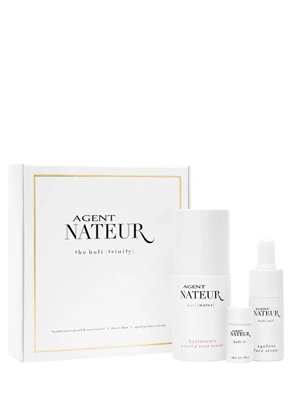 Beyaz bir arka plan üzerinde, Agent Nateur holi (trinity) yazılı şık beyaz bir kutu ve yanında üç adet beyaz seyahat boyu cilt bakımı ürünü şişesi; bunlar Agent Nateur holi (water) hyaluronik inci ve gül toneri, holi (oil) yaşlanma karşıtı yüz serumu ve holi (e) duo'dur.