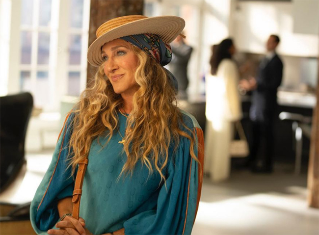 And Just Like That dizisinin başrolü Carrie Bradshaw, uzun dalgalı saçları, başındaki eşarplı açık renk hasır şapkası ve mavi, desenli geniş kollu bluzuyla kendine özgü eklektik stilini sergileyerek dizi kostümleri içinde şapkaların önemini vurguluyor.