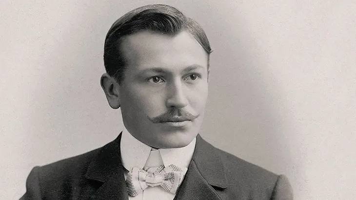 Rolex’in kurucusu Hans Wilsdorf’un gençlik yıllarına ait siyah-beyaz portresi; klasik takım elbise ve papyonuyla markanın vizyoner ruhunu yansıtan fotoğraf.