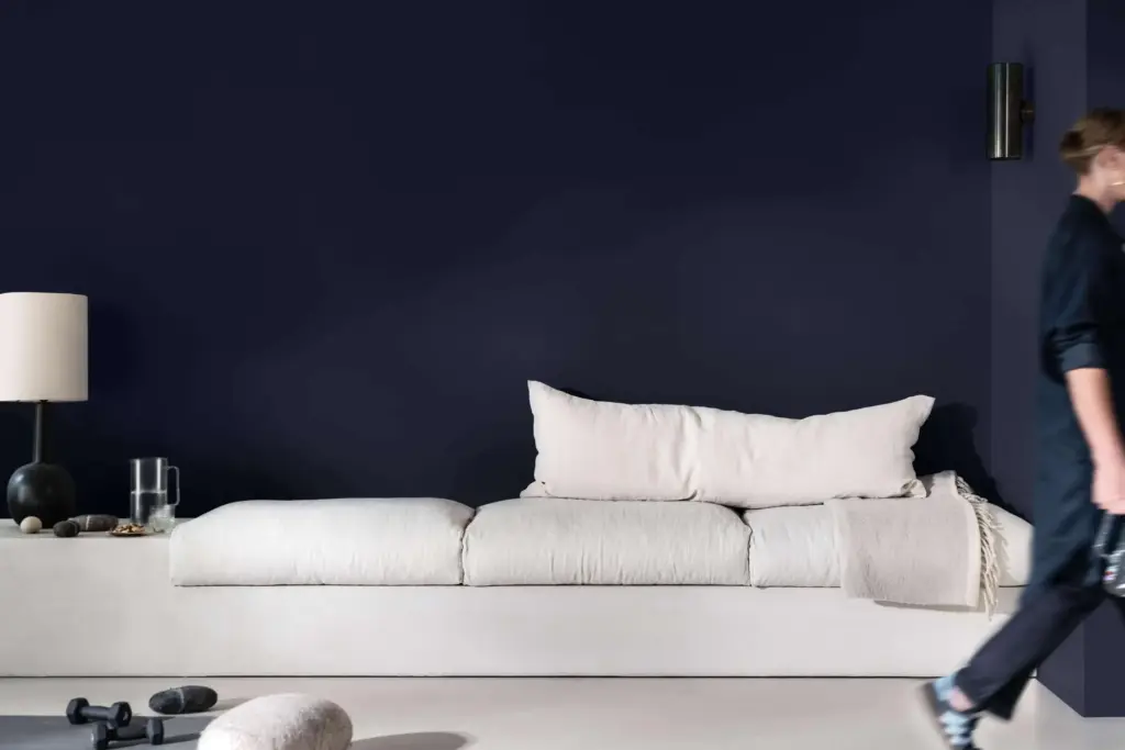 Koyu lacivert duvar, açık renk koltuk ve minimalist aksesuarlarla dekore edilmiş modern oturma alanı.