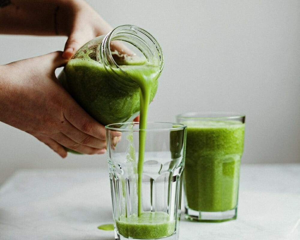 Kavanozdan bardağa dökülen taze hazırlanmış yeşil smoothie, sağlıklı yaşam ve detoks için doğal bir içecek.