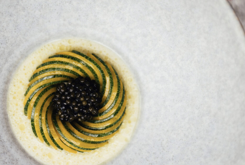 Kopenhag'ın özenle hazırlanmış gastronomi sahnesinden bir kesit sunan bu tabakta, ortasında parlak siyah havyarın, etrafında spiral şeklinde dizilmiş incecik yeşil ve sarı sebze dilimlerinin köpüklü hafif bir sosla buluştuğu, şehrin beğenilen restoranlarında rastlayabileceğiniz yaratıcı ve sanatsal bir lezzet sunumu yer alıyor.