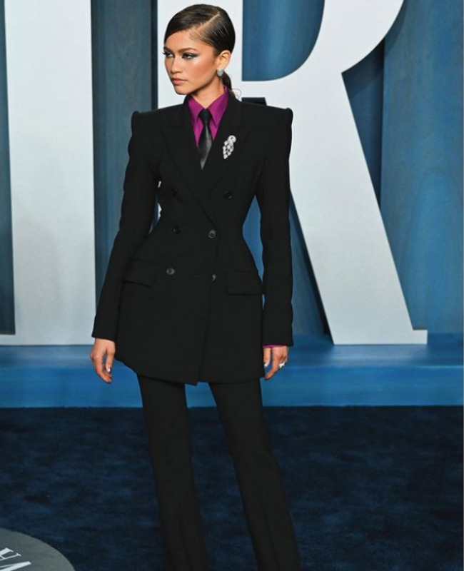 Stil ikonu Zendaya, 2022 Vanity Fair Oscar Partisi'nde giydiği, keskin hatlara sahip siyah kruvaze ceket ve pantolondan oluşan takımı, mor bir gömlek, ince siyah kravat ve yaka detayındaki ışıltılı broşuyla tamamlayarak maskülen tavrı elegant bir şekilde yansıtıyor.