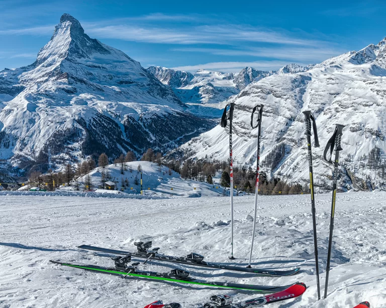 Zermatt’ta Matterhorn manzaralı kayak pistinde yerde duran kayak takımları ve kayak batonları, açık havada kış tatili atmosferi.