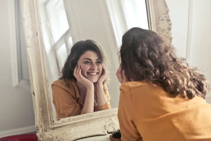 Aynaya bakarak neşeyle gülümseyen genç kadın.


