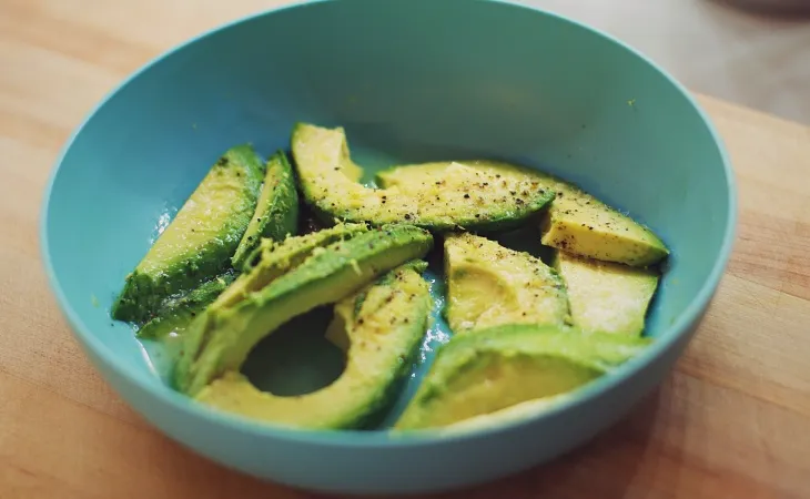 Bir kasede dilimlenmiş avokado üzerine serpilmiş baharatlarla hazırlanmış lezzetli ve sağlıklı vegan atıştırmalık.