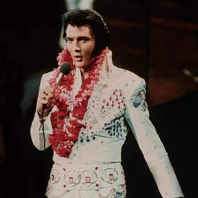 1973 Aloha from Hawaii konserinde sahne alan Elvis Presley, beyaz taşlı kostümü ve kırmızı lei çiçek kolyesiyle