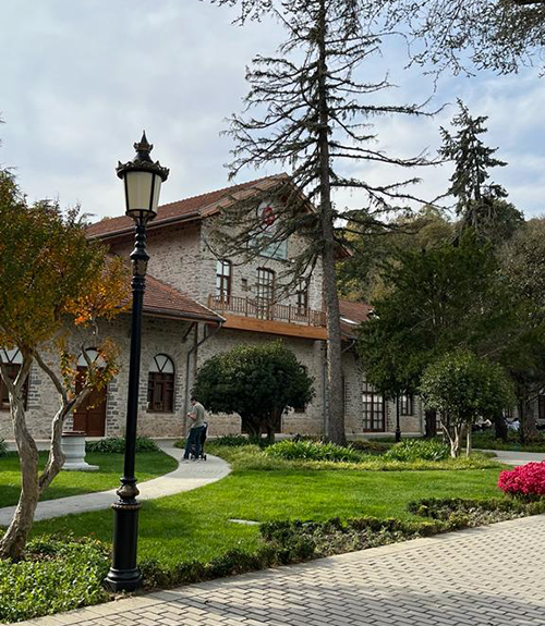 Kiremit çatılı, tarihi bir taş yapı olan Beykoz Cam Müzesi'nin önünde, zarif bir siyah sokak lambası, özenle düzenlenmiş yemyeşil bahçeler ve göğe uzanan ağaçlar bulunmaktadır, burası sakin bir atmosfer sunuyor.