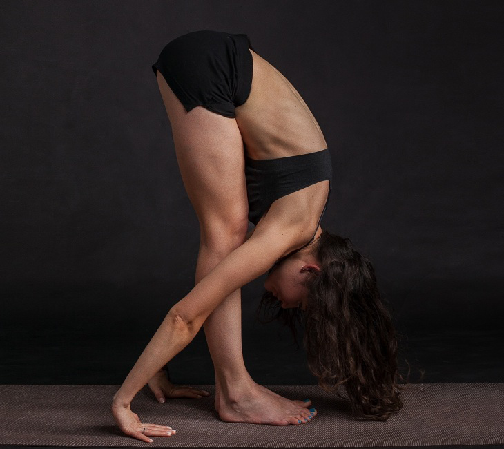 Siyah spor kıyafetleri içinde, uzun koyu renkli saçları mata değecek şekilde öne doğru derin bir eğilme yoga pozisyonu yapan bir kadın, zihni yavaşlatıp kaliteli uykuya yardımcı olan bilim destekli egzersiz ve rahatlama ipuçlarının önemini vurguluyor.