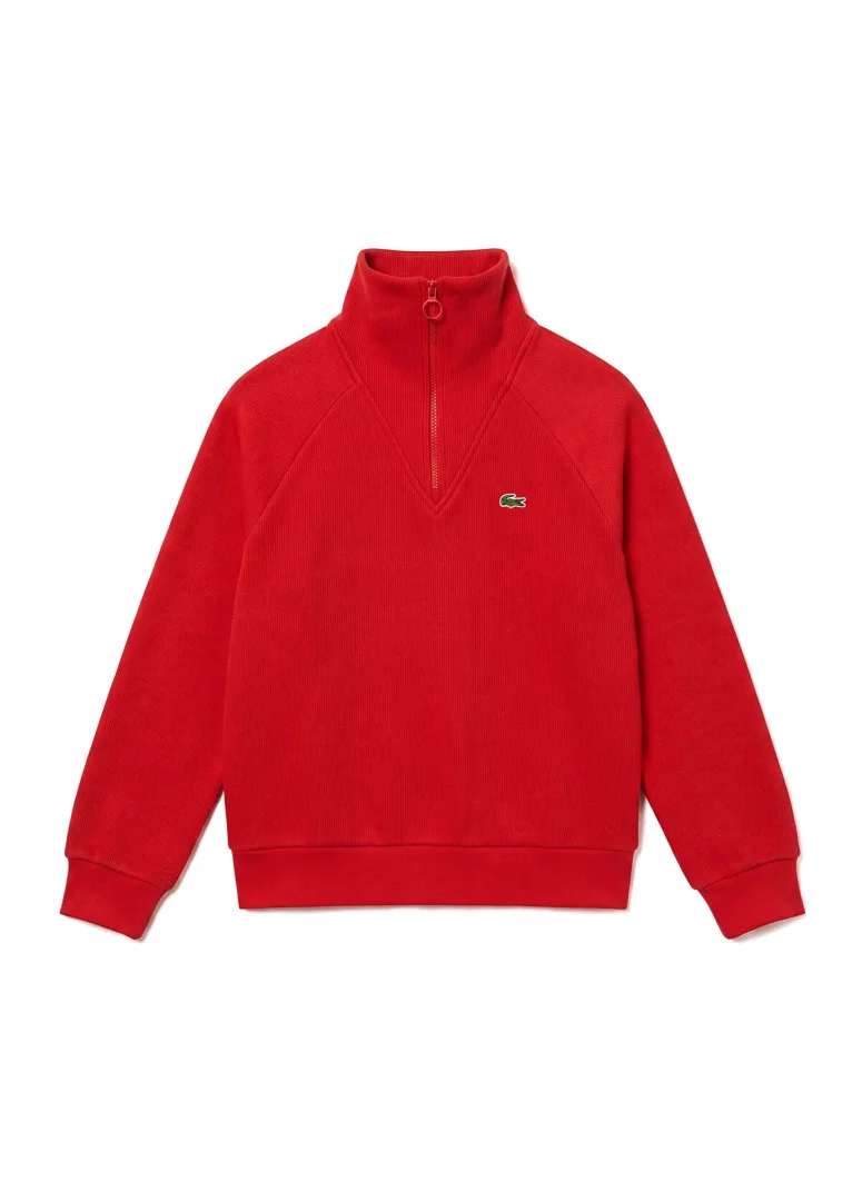 Beyaz arka plan üzerinde duran, dik yakalı ve çeyrek fermuarlı, reglan kollu, fitilli kumaş dokusuna sahip parlak kırmızı renkli sweatshirt, sol göğsünde yeşil timsah logosuyla sportif stilin modern bir yorumunu sunuyor.