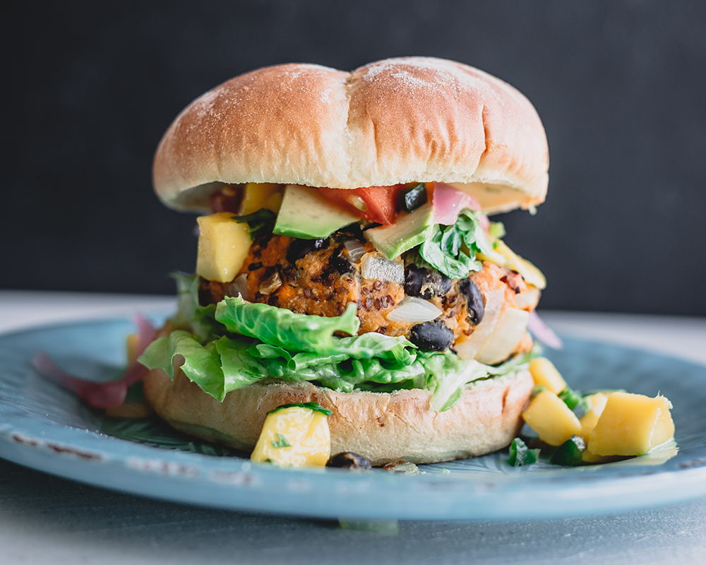 Sebzeler, baklagiller ve mango dilimleriyle hazırlanan, sağlıklı ve lezzetli görünüme sahip vegan burger.