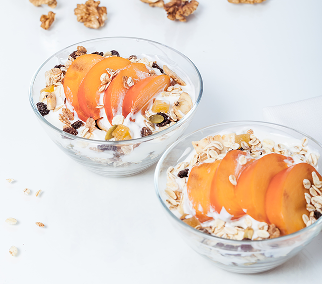 İki cam kasede, dilimlenmiş hurma, vegan yoğurt ve granola karışımıyla hazırlanan sağlıklı kahvaltı veya ara öğün alternatifi.