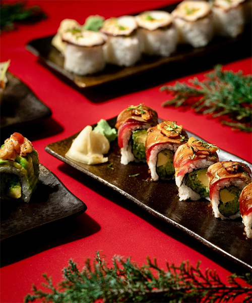 Canlı kırmızı bir zemin üzerinde, özenle hazırlanmış farklı çeşitlerdeki sushi roll'lar, yanında wasabi ve zencefil turşusu ile modern dokunuşlarla sunulmuş, İstanbul'un en popüler sushi restoranlarında tadabileceğiniz taze ve özgün lezzetleri temsil ediyor.