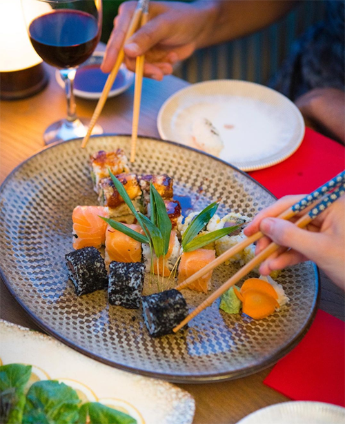 Birbirinden farklı somonlu, koyu renkli ve soslu çeşitleriyle özenle hazırlanmış bir tabak dolusu sushinin önünde, iki kişinin çubuklarla keyifle sushi seçtiği bu detaylı görüntü, İstanbul’un en iyi sushi restoranlarındaki zengin Uzak Doğu mutfağı deneyimini yansıtıyor.