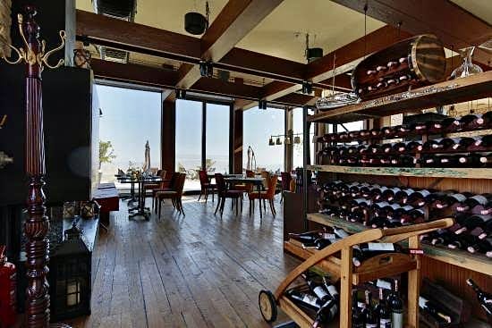 Kapadokya'nın eşsiz manzarasını içeri taşıyan geniş pencereleri, ahşap zeminleri ve tavan kirişleriyle sıcak bir atmosfere sahip bu şık yemek mekanında, çeşitli şarap şişeleriyle dolu büyük raflar ve zarifçe düzenlenmiş masalar, misafirlerini bekliyor.