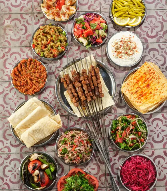 Ciğerci Baba'nın masasında, ızgara ciğer şişlerin çevresini saran kırmızı lahana, gavurdağı, közlenmiş sebzeler, acılı ezme, patlıcan salatası, haydari ve limon dilimli turşu biber gibi birçok taze ve lezzetli mezenin sunulduğu bu görsel, Samsun'un beğenilen mekanlarından birinin zengin ikram anlayışını gözler önüne seriyor.