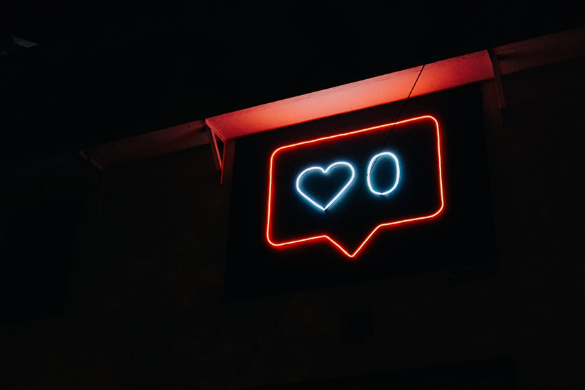 Siyah bir arka planda, kırmızı çerçeveli bir sosyal medya beğeni bildirimi içinde neon maviyle yazılmış '0' ve kalp simgesi yer alıyor; sosyal medyada ilgi görmeme teması öne çıkıyor.
