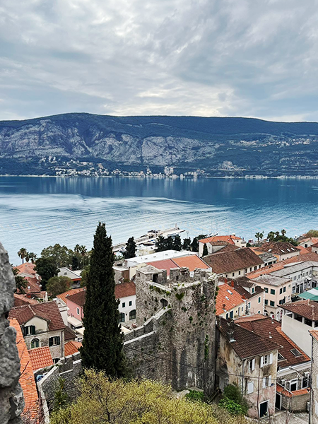 Kanlı Kula'nın taştan duvarlarının ve eski kiremit çatılı evlerin gözüktüğü bu kuşbakışı manzarada, Herceg Novi şehrinin dik yamaçlarından Kotor Körfezi'nin berrak suları ve uzaktaki dramatik Karadağ dağları, Adriyatik'in eşsiz güzelliğini bulutlu bir havada bile gözler önüne seriyor.