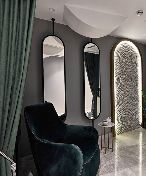 Karadağ seyahat rehberiniz için şık bir konaklama alternatifi sunan La Fleur Boutique Hotel'in zarif tasarım detaylarını yansıtan bu karede, koyu zümrüt yeşili kadife koltuk, tavandan asılı modern aynalar, yuvarlak mozaik desenli niş ve aydınlatma ile kişisel ve rafine bir atmosfer vurgulanıyor.
