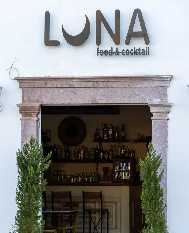 Beyaz cepheli, taş çerçeveli girişinde ay şekilli U harfiyle LUNA food & cocktail tabelasının bulunduğu Cunda Luna, Ayvalık Rehberi'nde öne çıkan keyifli mekanlardan biri; kapının iki yanında yükselen yeşil fidanlar ve içerideki bol çeşitli bar görüntüsüyle davetkar bir atmosfer sunuyor.