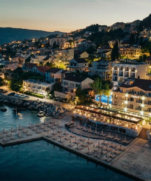Gün batımının ardından ışıklarla parlayan Karadağ'ın Herceg Novi şehrinde, denize sıfır konumlanmış Hotel Perla'nın uzanan platform plajı, şemsiyelerle donatılmış şezlongları ve körfez manzaralı restoranı, Adriyatik Denizi'nin huzurlu atmosferiyle bütünleşiyor.
