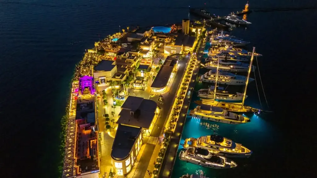 Türkiye'nin en güzel marinalarından birinin gece kuşbakışı görüntüsü; ışıltılı binaları, lüks yatları, teknelerin altında parlayan turkuaz suları ve hareketli sosyal alanlarıyla dikkat çekiyor.
