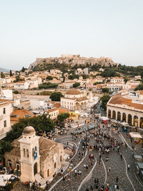Atina'nın hareketli Monastiraki Meydanı'ndan yükselen Akropolis'in etkileyici silüetini gözler önüne seren bu kalabalık şehir manzarası, Yunanistan'ın tarihi dokusunu ve yaz tatili için cazip ev kiralama fırsatlarını keşfetmeye davet ediyor.