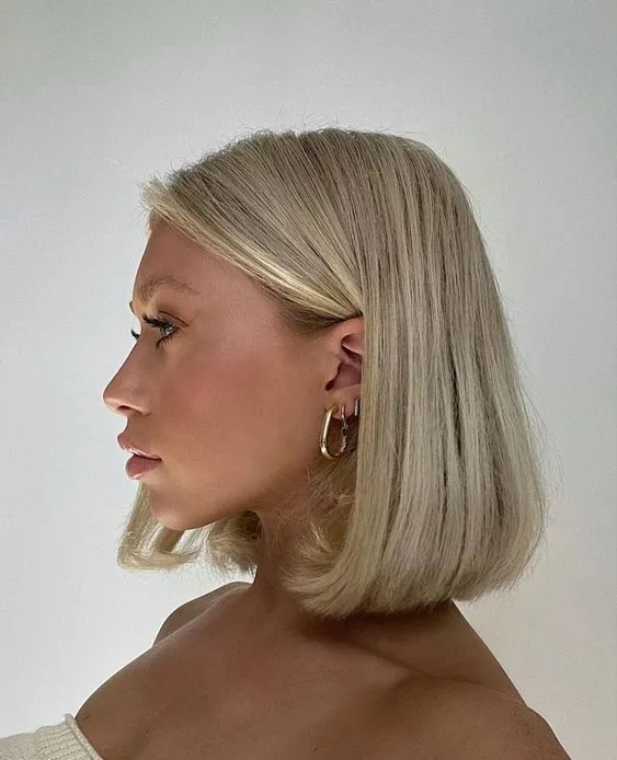 Yandan görünen, modern ve sofistike bir kısa küt saç modeline sahip genç bir kadın, açık sarı renkteki çene hizasındaki düz kesilmiş saçlarıyla poz veriyor; bu küt saç modeli, stilinize kattığı zarif ve sağlıklı görünümle her zaman tercih edilen seçeneklerden biridir, şıklığıyla öne çıkıyor.