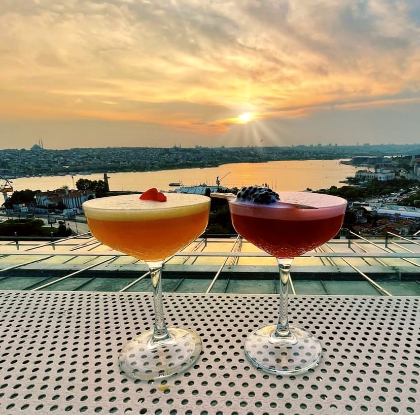İstanbul Boğazı üzerindeki nefes kesen gün batımı manzarasına karşı bir teras masasında duran, turuncu renkli üzeri kalp şeklinde bir çilekle süslenmiş bir kokteyl ve koyu kırmızı renkli üzeri böğürtlenlerle süslenmiş bir diğer kokteyl, şehrin en iyi teraslı mekânlarında yaşanacak keyifli anlara çağrı yapıyor.