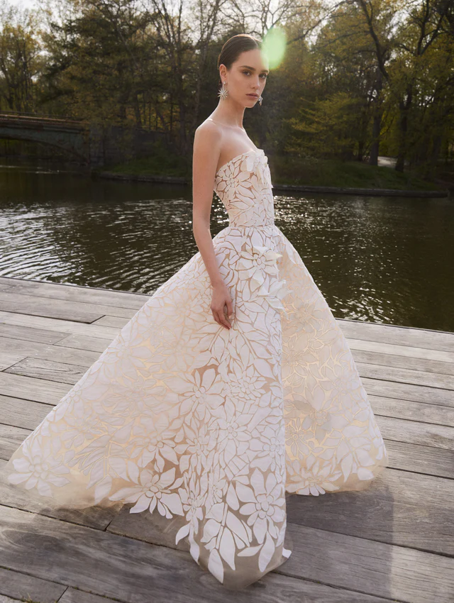 Oscar de la Renta 2025 koleksiyonundan, altın tonlu astarlı ve lazer kesim çiçek desenli straplez gelinlik modeli.