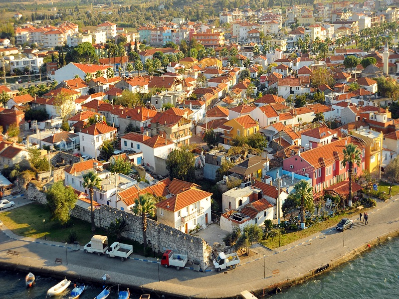 Sığacık'ın tarihi dokusunu yansıtan, denize nazır konumlanmış kırmızı kiremitli çatılara sahip şirin evleri, kıyı boyunca uzanan güçlü kale duvarları ve masmavi limanında demirli tekneleriyle pitoresk bir kuşbakışı manzara.
