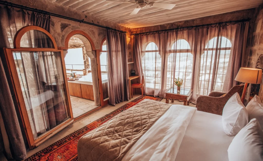 Geniş pencerelerden ışık alan, taş duvarları ve rustik dekorasyonuyla dikkat çeken Argos in Cappadocia otel odası.