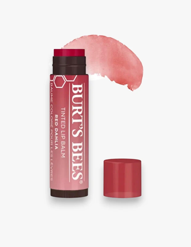 Beyaz arka plan üzerinde konumlandırılmış, kapağı yanında duran koyu kırmızı renkli Burt's Bees Tinted Lip Balm Red Dahlia dudak nemlendiricisi ve ürünün dudağa kattığı açık şeftali-pembe tonunu gösteren bir renk örneği.
