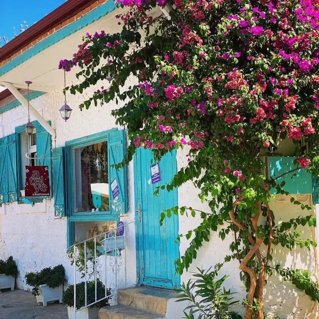 Datça'nın doğal dokusunu yansıtan, mor ve pembe begonvillerle sarılı, turkuaz panjurlu ve kapılı beyaz badanalı bir yapı, Ege ile Akdeniz'in buluştuğu bu eşsiz noktada sakin yaşamın ve yerel estetiğin bir örneğini sunuyor.