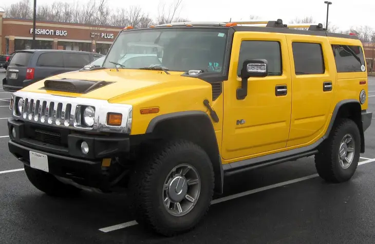 Bu dikkat çekici parlak sarı Hummer H2 modeli, kendine özgü krom ızgarası, kaput üzerindeki hava girişi ve sağlam arazi lastikleriyle, Hummer markasının tarihinin ve çeşitli modellerinin önemli bir parçası olarak asfalt bir otoparkta park edilmiş duruyor.