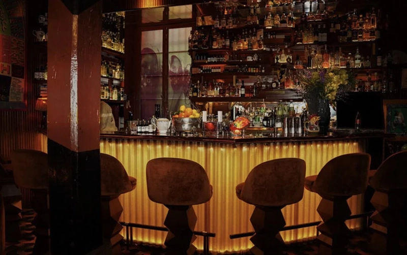 Loş ışıklı, altın rengi detaylara sahip, arkasında çok sayıda içki şişesi bulunan ve özel tasarımlı kadife bar tabureleriyle davetkar bir atmosfer sunan bu şık Paris barı, En İyi Paris Restoranları arasında yer alan zarif bir mekanın akşamüstü veya gece halini yansıtıyor.