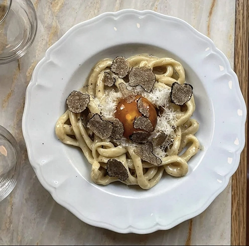 Paris'in en iyi restoranlarında sunulan zengin gastronomik deneyimleri yansıtan bu beyaz, dalgalı kenarlı tabakta, bolca rendelenmiş siyah trüf mantarı ve taze yumurta sarısı ile zenginleştirilmiş kremalı soslu özel bir makarna tabağı göz alıcı bir şekilde duruyor.