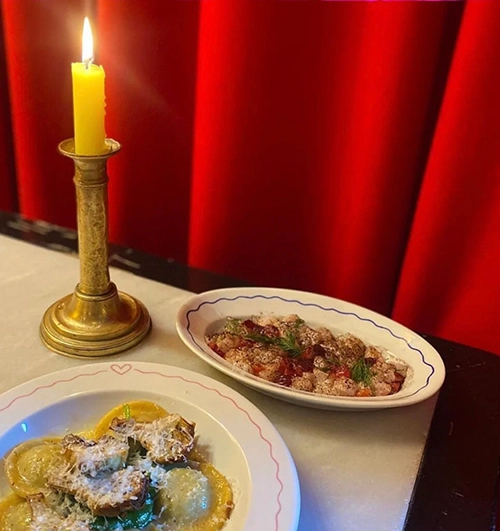 Paris restoranlarının samimi ve şık atmosferini yansıtan bu karede, yanan mum ışığında servis edilen, parmesan peyniri ve mantarlarla zenginleştirilmiş taze makarnanın ve yanında soslu bir deniz ürünü başlangıcının enfes lezzetleri davetkar kırmızı bir fon önünde masayı süslüyor.