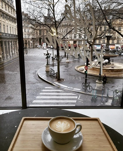 Islak Paris sokaklarına ve klasik binalara bakan bir pencerenin önünde, ahşap tepsideki kalp desenli latte, En İyi Paris Restoranları listesindeki Cafe Kitsuné gibi mekanlarda güne keyifli bir başlangıç için ideal bir manzarayı sunuyor.