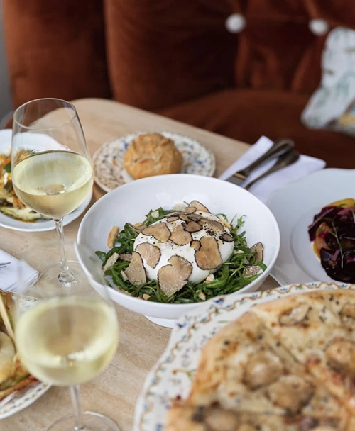 Paris'in en iyi restoranlarından birinde, üzerinde bol trüf mantarı dilimi ve çam fıstığı bulunan kremalı burrata salatasının taze roka yatağında servis edildiği, iki kadeh beyaz şarap ve diğer lezzetlerle dolu bir masada sunulan şık gastronomi deneyimi.