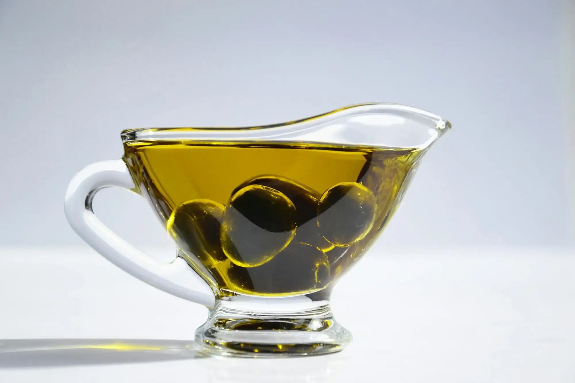 Cam kap içinde zeytin taneleriyle birlikte sunulan sızma zeytinyağı, berrak dokusu ve altın rengiyle kaliteli zeytinyağı görünümü