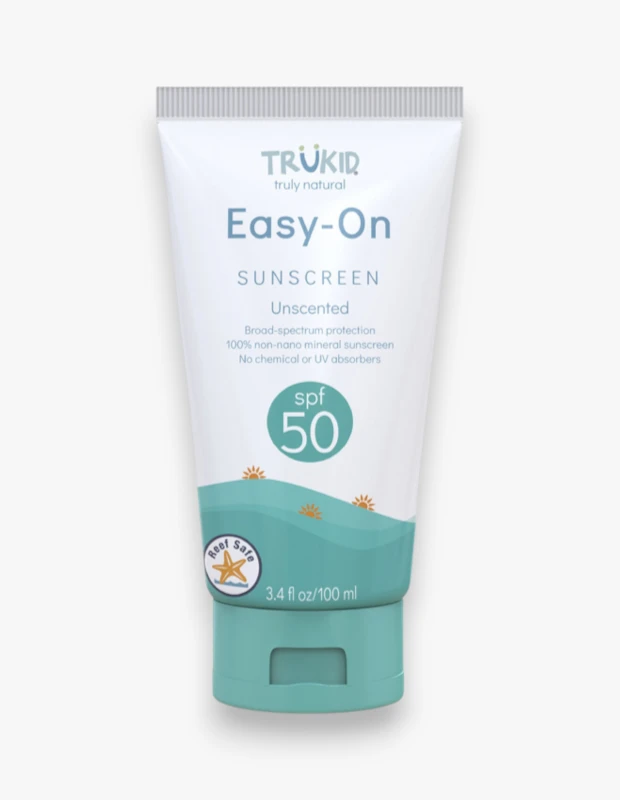 Beyaz bir arka plan üzerinde dikey duran, üst kısmı beyaz, alt kısmı deniz yeşili dalgalı desenli TRŪKID Easy-On Güneş Kremi SPF 50 tüpü, mercan resifleri için güvenli olduğunu belirten bir logo ve kokusuz formülü ile öne çıkıyor.