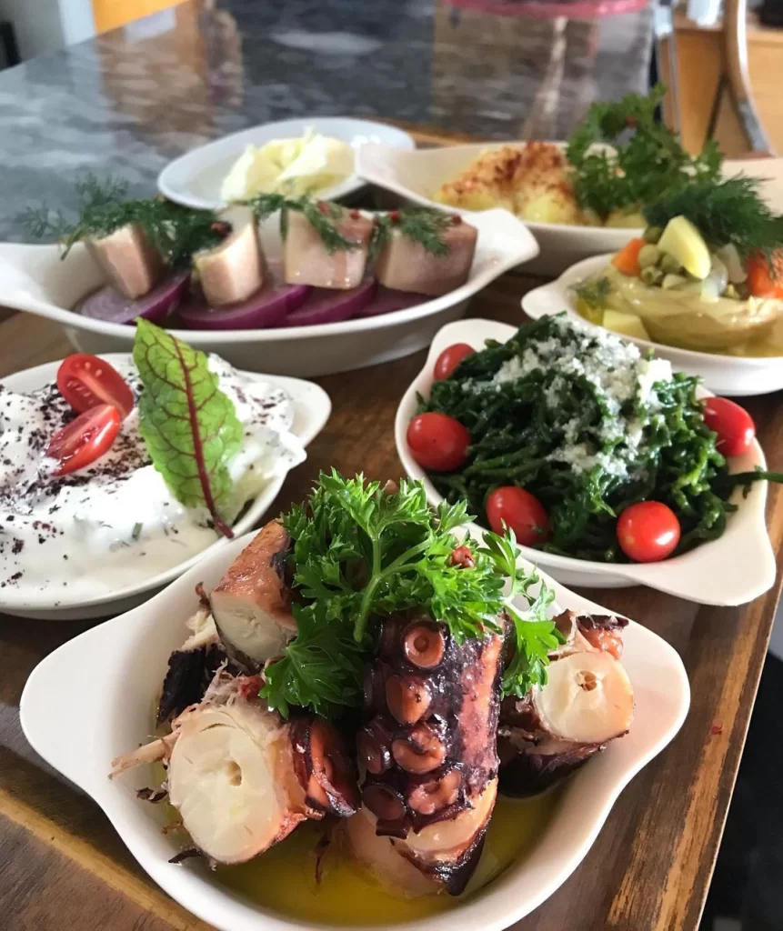 Restoran masasında, taze maydanozlu ve zeytinyağında ızgara ahtapot, çeri domatesli ve peynirli deniz börülcesi, sumaklı yoğurtlu sos, dereotlu salamura balık dilimleri ve enginar gibi birçok çeşitli ve iştah açıcı Akdeniz mezeleri görsel bir şölen sunuyor.