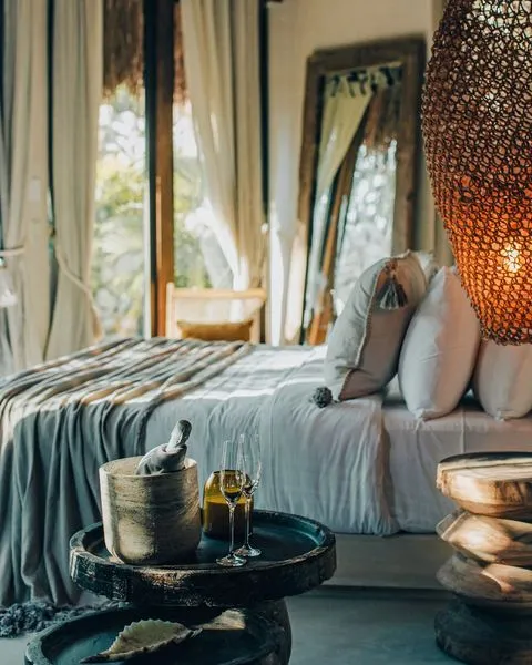Hotel Muaré Tulum'un tropikal yeşilliklerle çevrili odasında, yumuşak ışığın süzüldüğü bembeyaz çarşaflı bir yatağın yanında, ahşap sehpada serinletici içecekler ve kadehlerle bezenmiş bu alan, balayı çiftleri için sakin ve romantik bir kaçamak sunan en güzel balayı rotaları arasında.