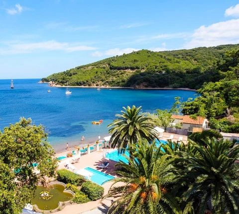 Elba Adası'ndaki Hotel Villa Ottone'un kuşbakışı görüntüsünde, masmavi Portoferraio körfezinde yüzen tekneler, palmiye ağaçları arasında yer alan havuzlar, şezlonglu özel plaj ve yemyeşil tepelerle çevrili bu romantik balayı rotası büyüleyici bir tatil vadediyor.