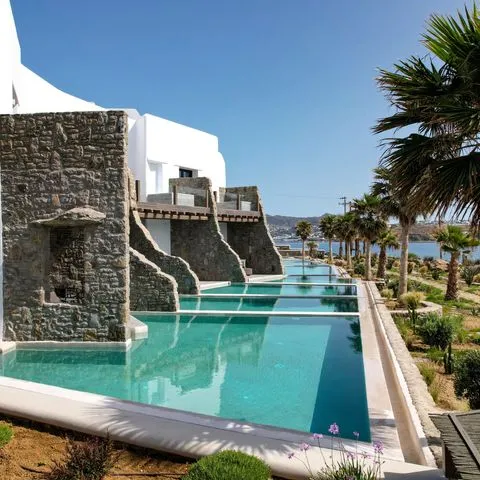 Denize nazır yemyeşil bir yamaçta, Mikonos'un bembeyaz mimarisine taş dokunuşlarla harmanlanmış, birbirini takip eden turkuaz sonsuzluk havuzları ve özel teraslara sahip Aeonic Suites & Spa otel, Ege'nin büyüleyici atmosferinde lüks bir tatil deneyimi sunuyor.
